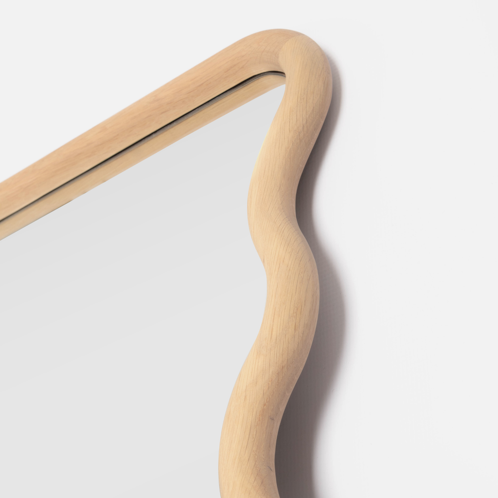 Close up of a solid oak wavy mirror on a light grey background